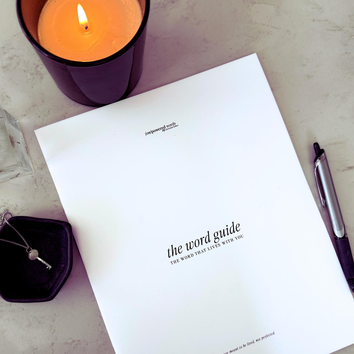 Notebook titled 'the word guide' with a lit candle and pen on a surface